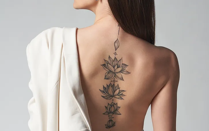 schmerzhaftesten-zonen-bei-taetowierungen-wirbelsaeule Eine weibliche Person mit vielen Blütentattoos auf der Wirbelsäule